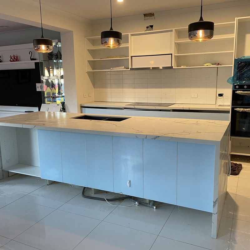 Kitchen island with a white marble-look stone top under pendant lights